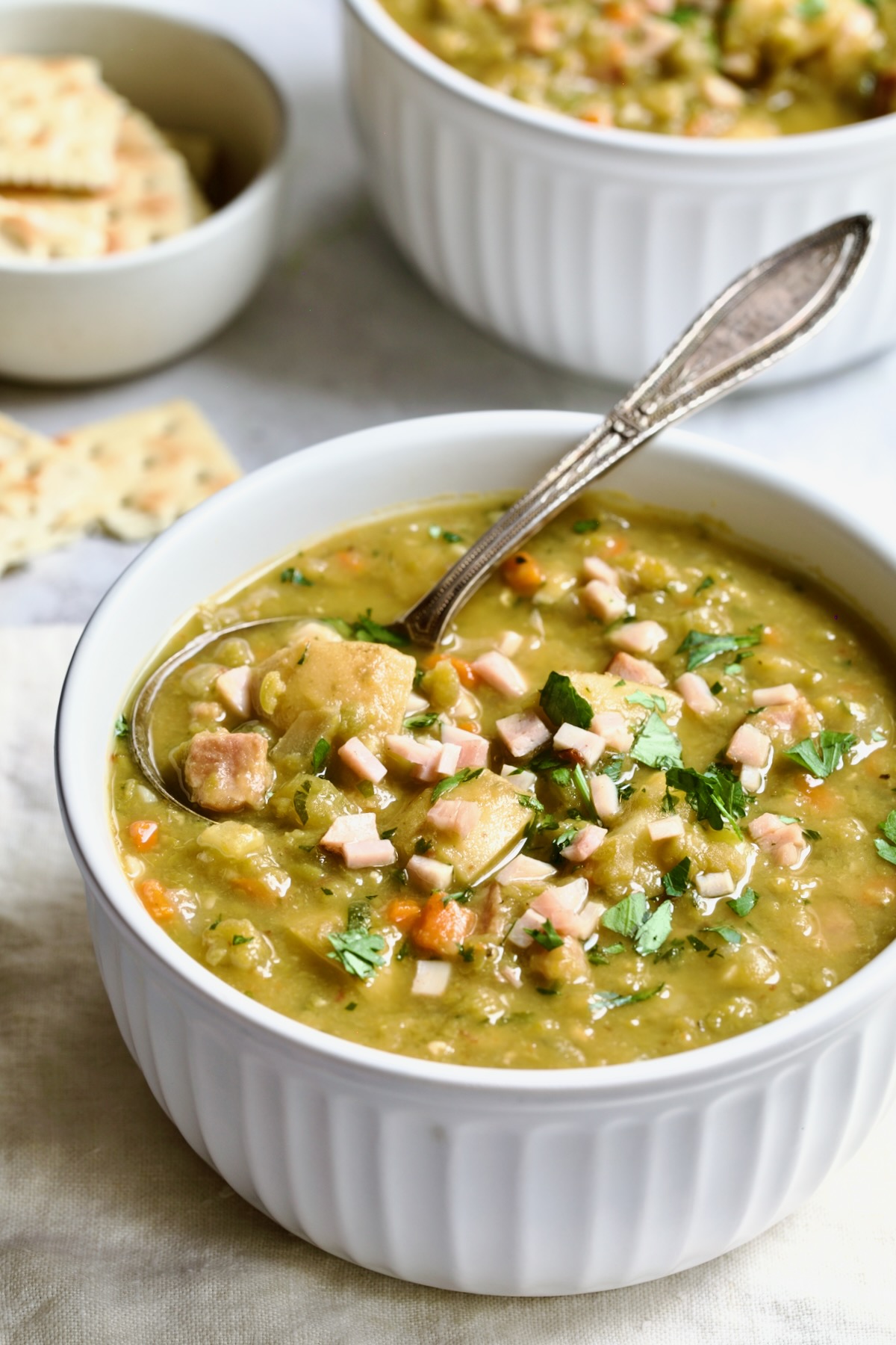 One serving of Slow Cooker Split Pea Soup in white bowl with spoon.