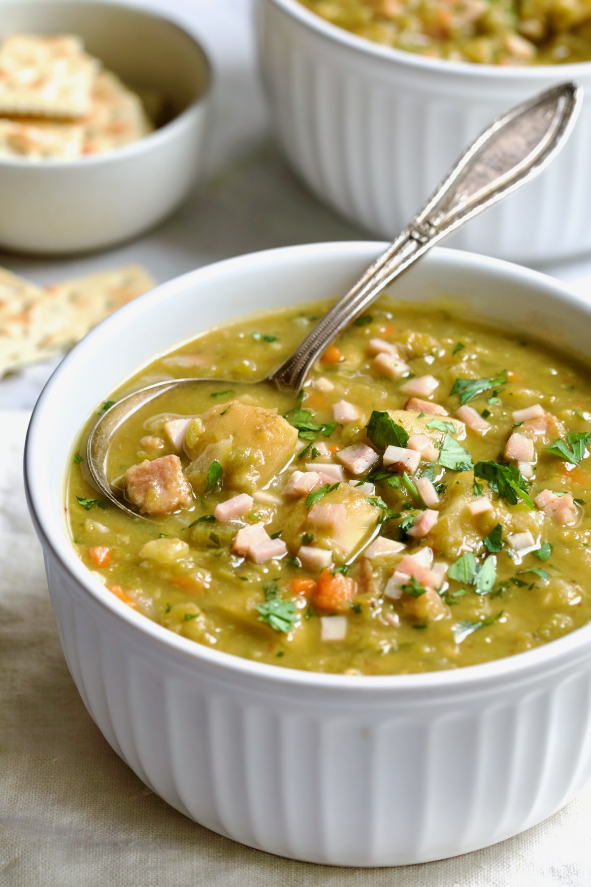 One serving of Slow Cooker Split Pea Soup in a white bowl with soup spoon.