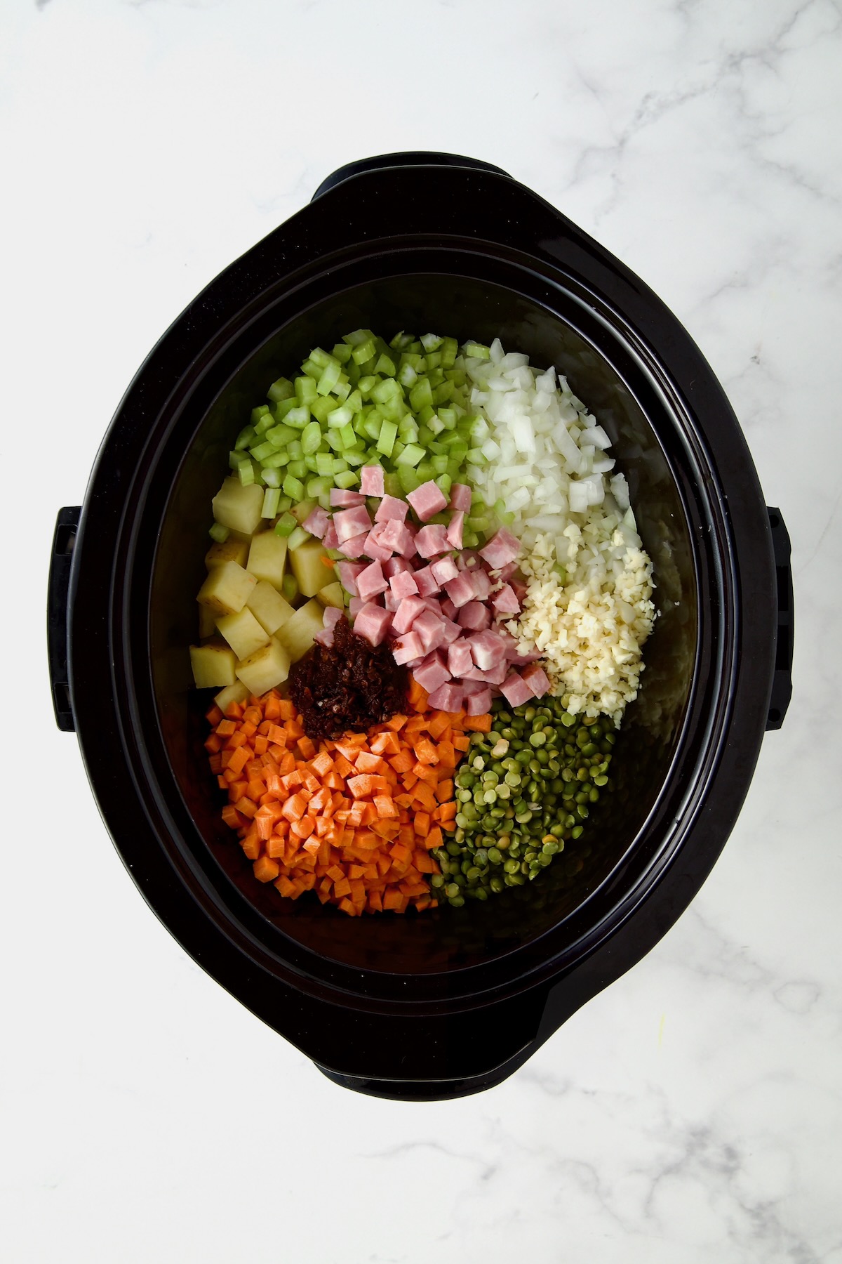 Diced vegetables and ham in black slow cooker before being mixed together.