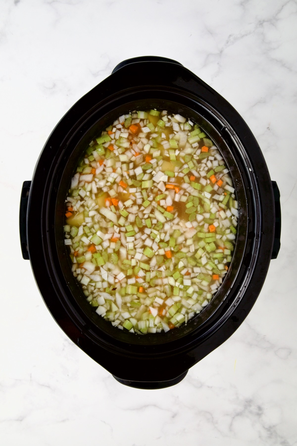 Diced vegetables and ham in black slow cooker before being mixed together with chicken broth added.