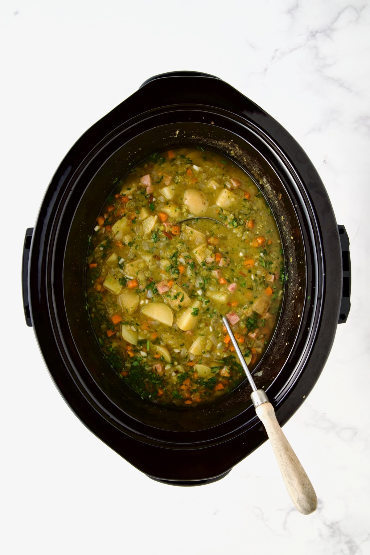 Slow Cooker Split Pea Soup in black slow cooker after being cooked with soup ladle.