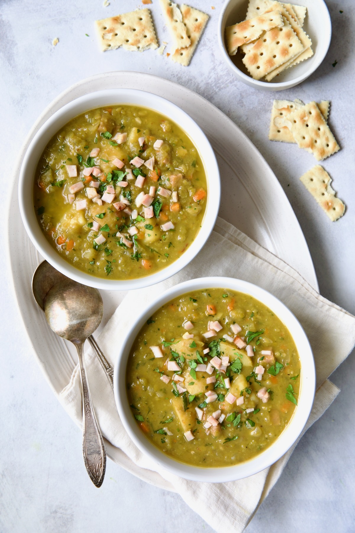 Two individual servings of Slow Cooker Split Pea Soup in white bowls on oval white platter.