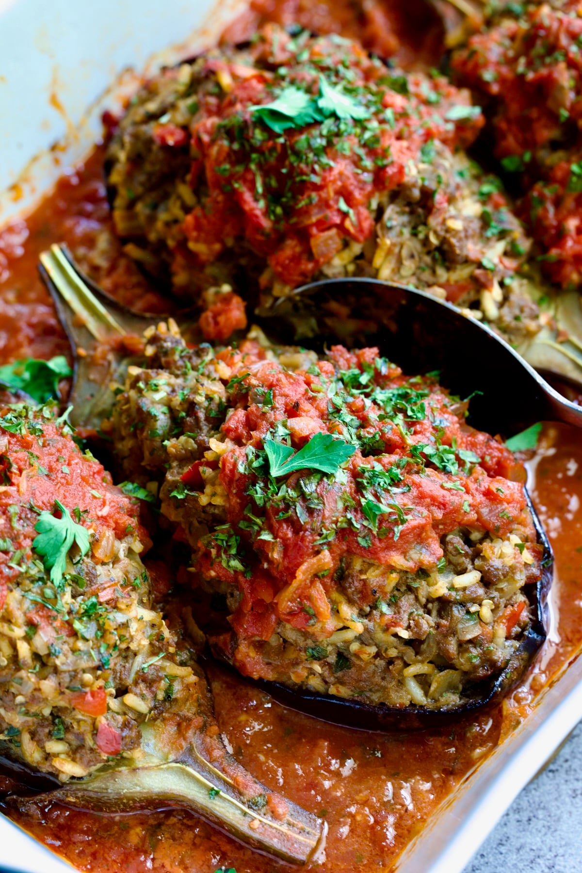 Three baked Stuffed Eggplant halves in white rectangular baking dish with serving spoon.