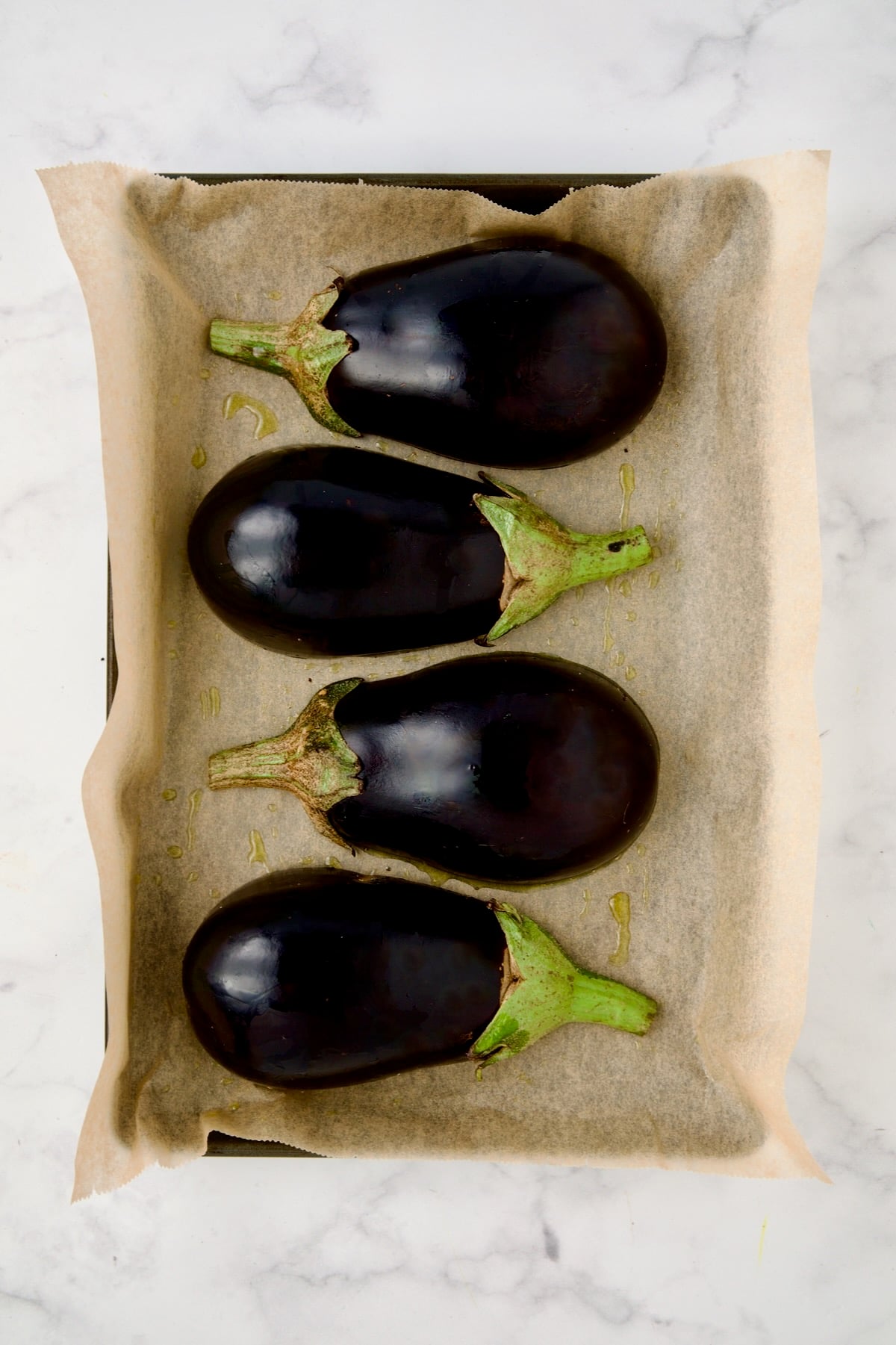 Four eggplant halves with skin side up on parchment paper lined rimmed baking sheet.