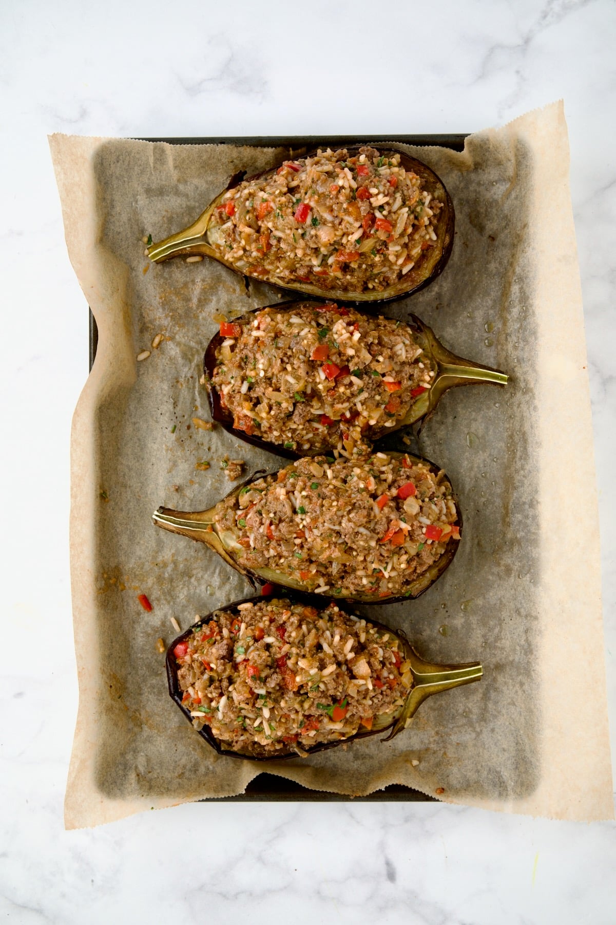 Four stuffed eggplant halves on parchment paper lined baking sheet ready to go into baking pan.