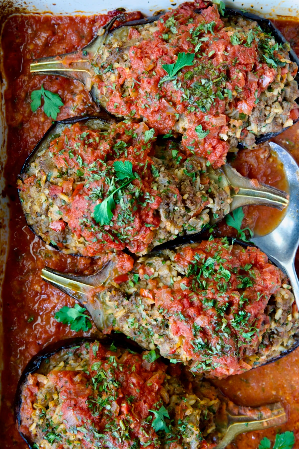 Four baked Stuffed Eggplant halves in white rectangular baking dish with serving spoon.