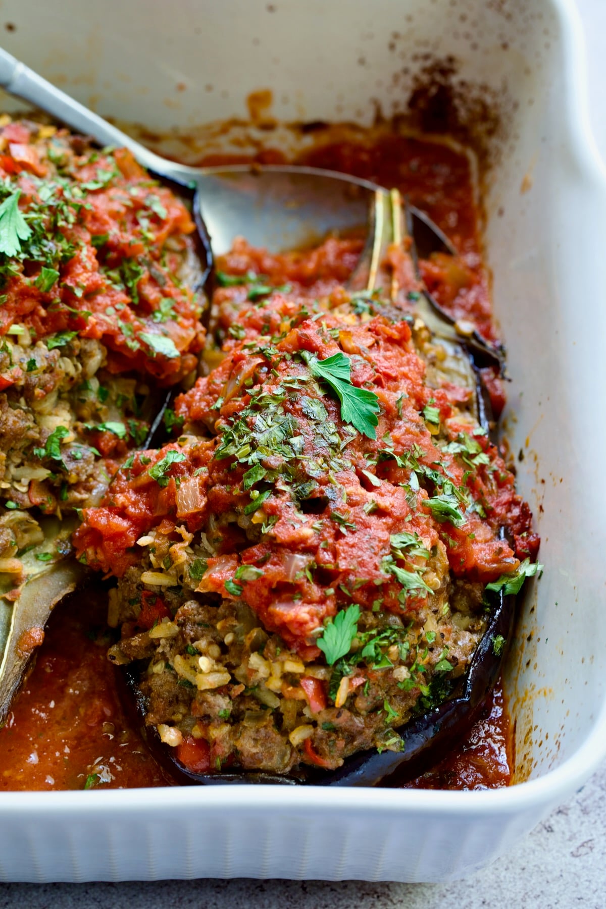 Close-up of one Stuffed Eggplant in white rectangular baking dish with serving spoon.