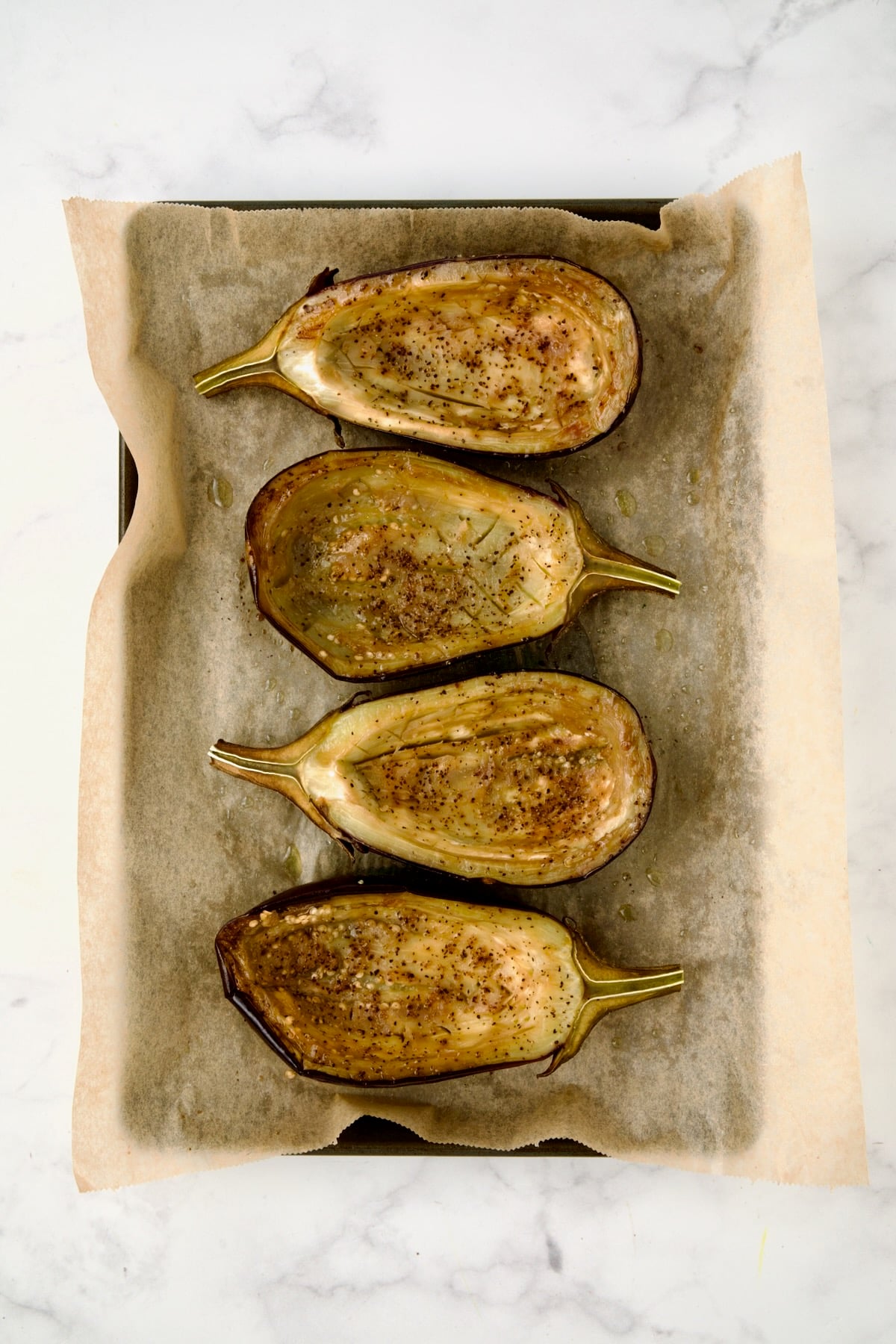 Four baked eggplant halves with pulp side up after being baked on parchment paper lined baking sheet.