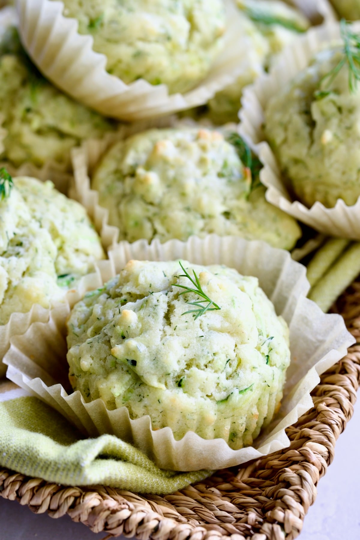 Pile of Dill Zucchini and Ricotta Muffins on square rattan basket.