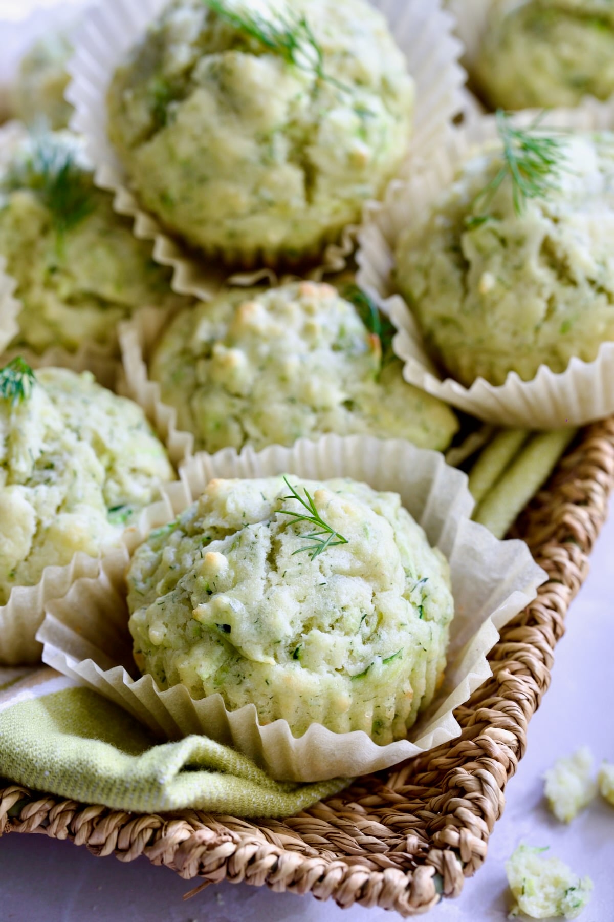 Pile of Dill Zucchini and Ricotta Muffins on square rattan basket.
