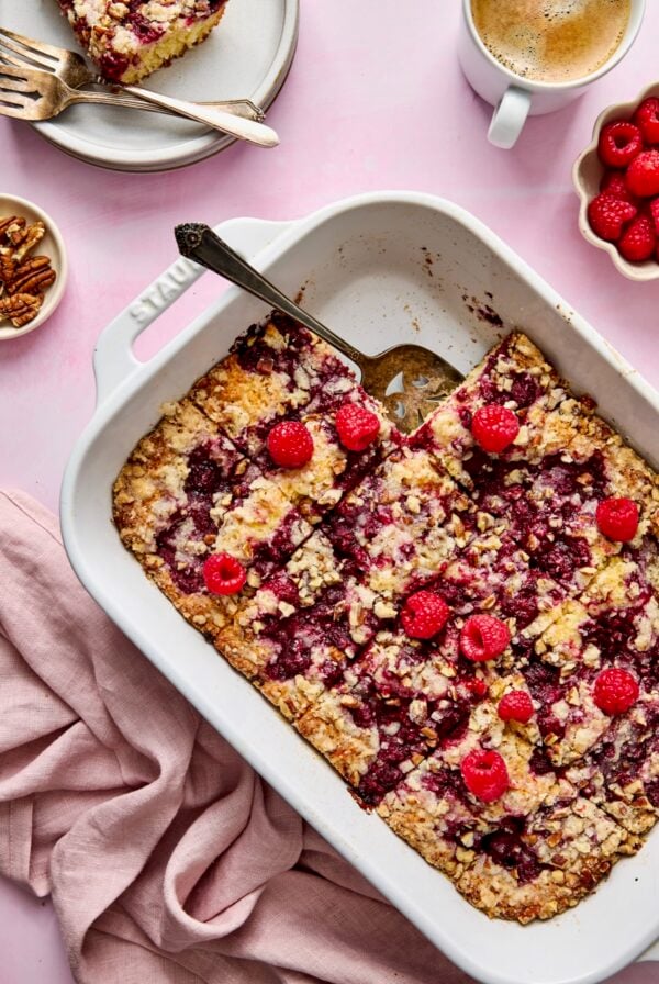 Easy Raspberry Coffee Cake in white rectangular baking dish cut into pieces with one removed onto a plate.