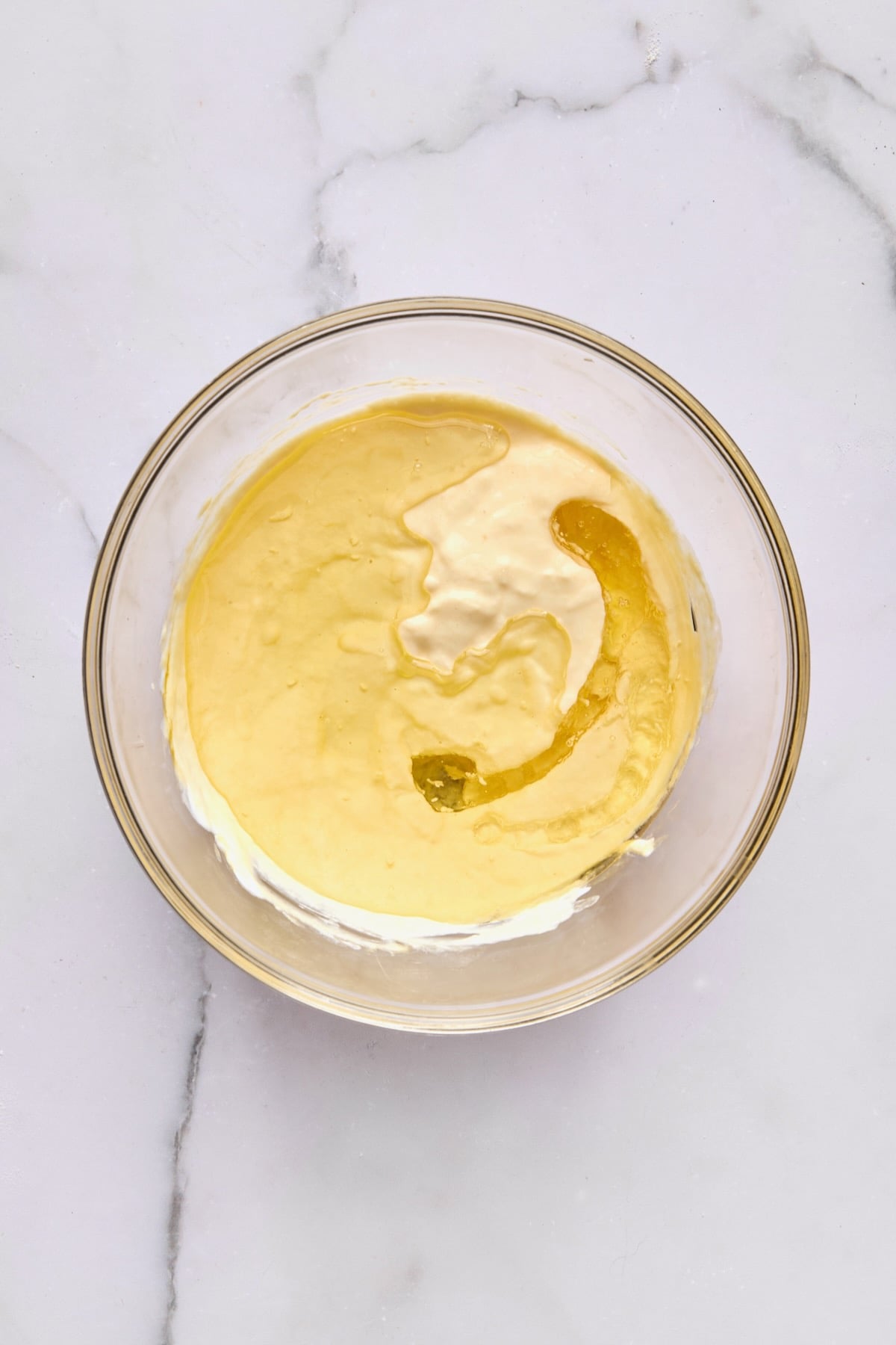Wet ingredients for coffee cake in glass bowl with yogurt and oil added.