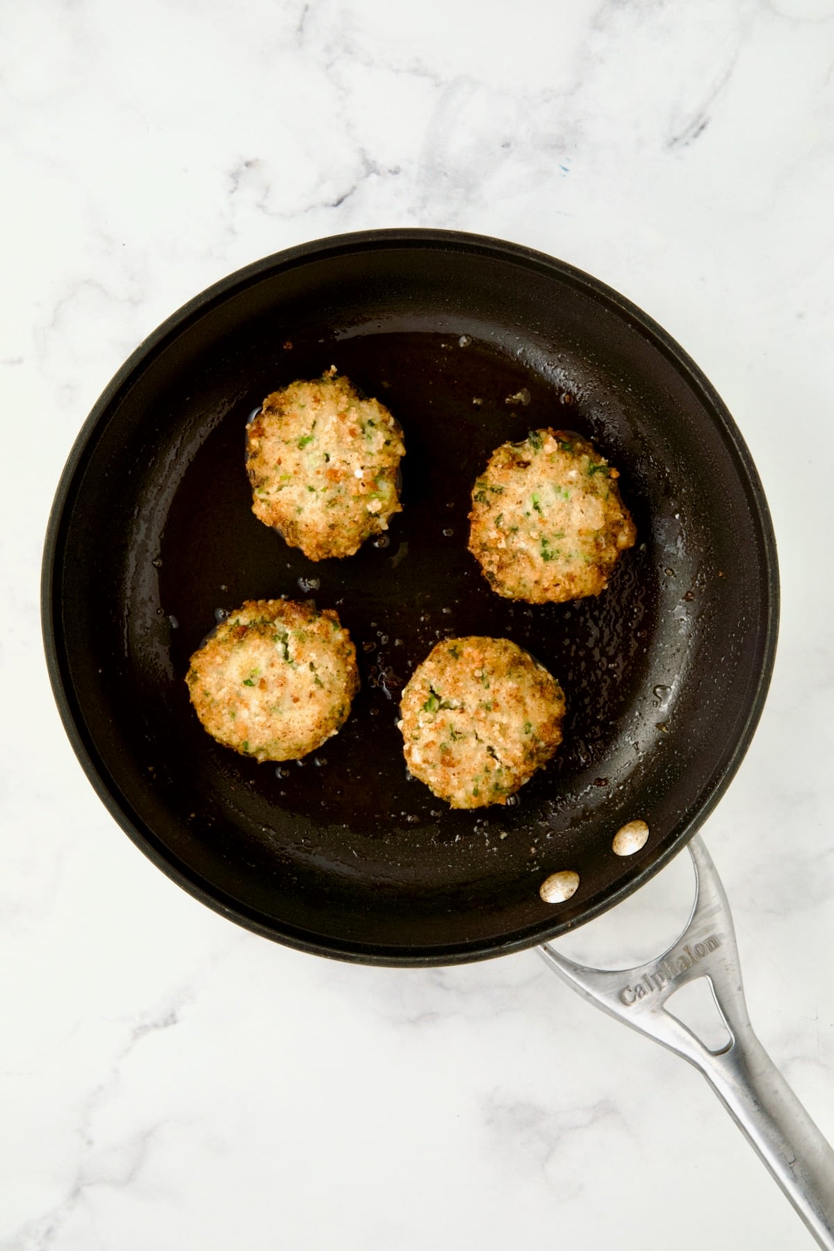 Four cooked shrimp cakes in nonstick skillet.