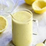 Creamy Lemon Dressing in glass pitcher surrounded by lemon halves.