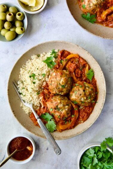 Three Harissa Chicken Meatballs with couscous in earthenware bowl.