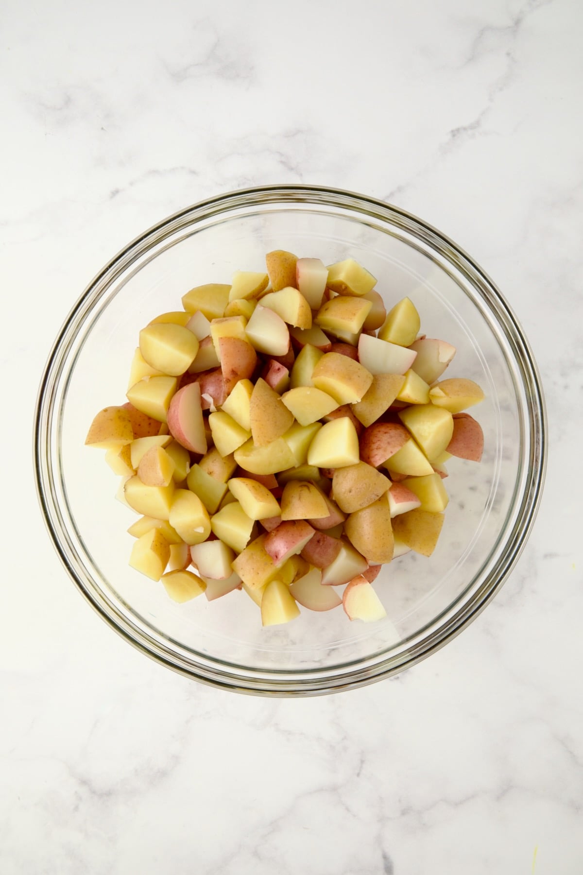 Cubed cooked red and yellow potatoes in glass bowl.