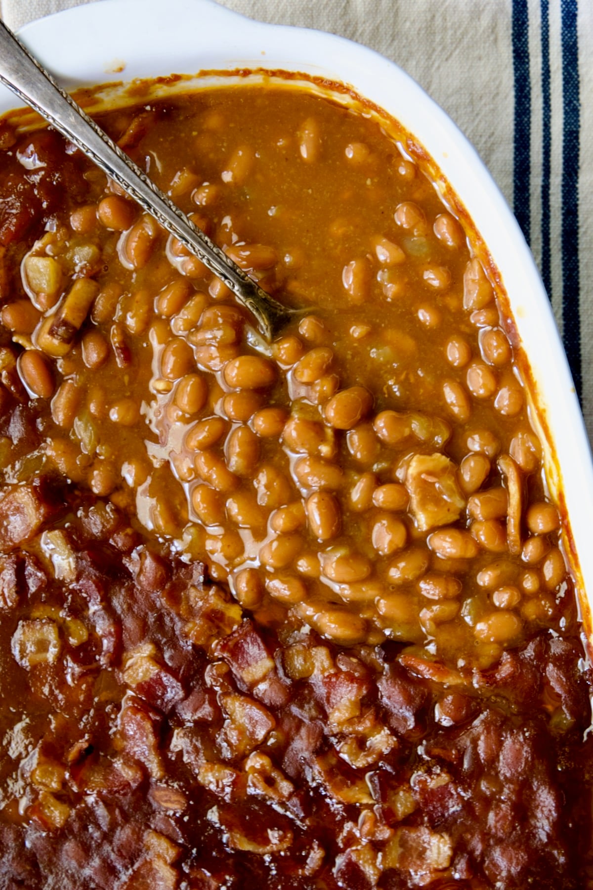 Best Canned Baked Beans Recipe in oval white baking dish with serving spoon.