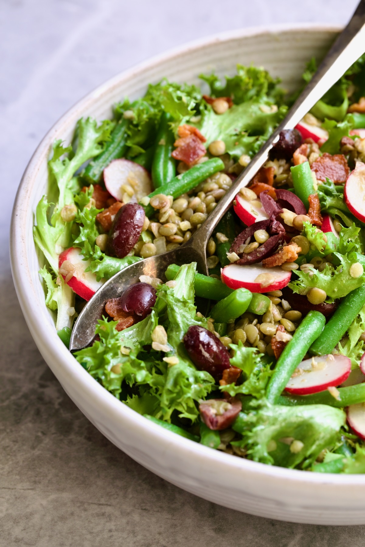 French Lentil Salad in white serving bowl with serving utensils.