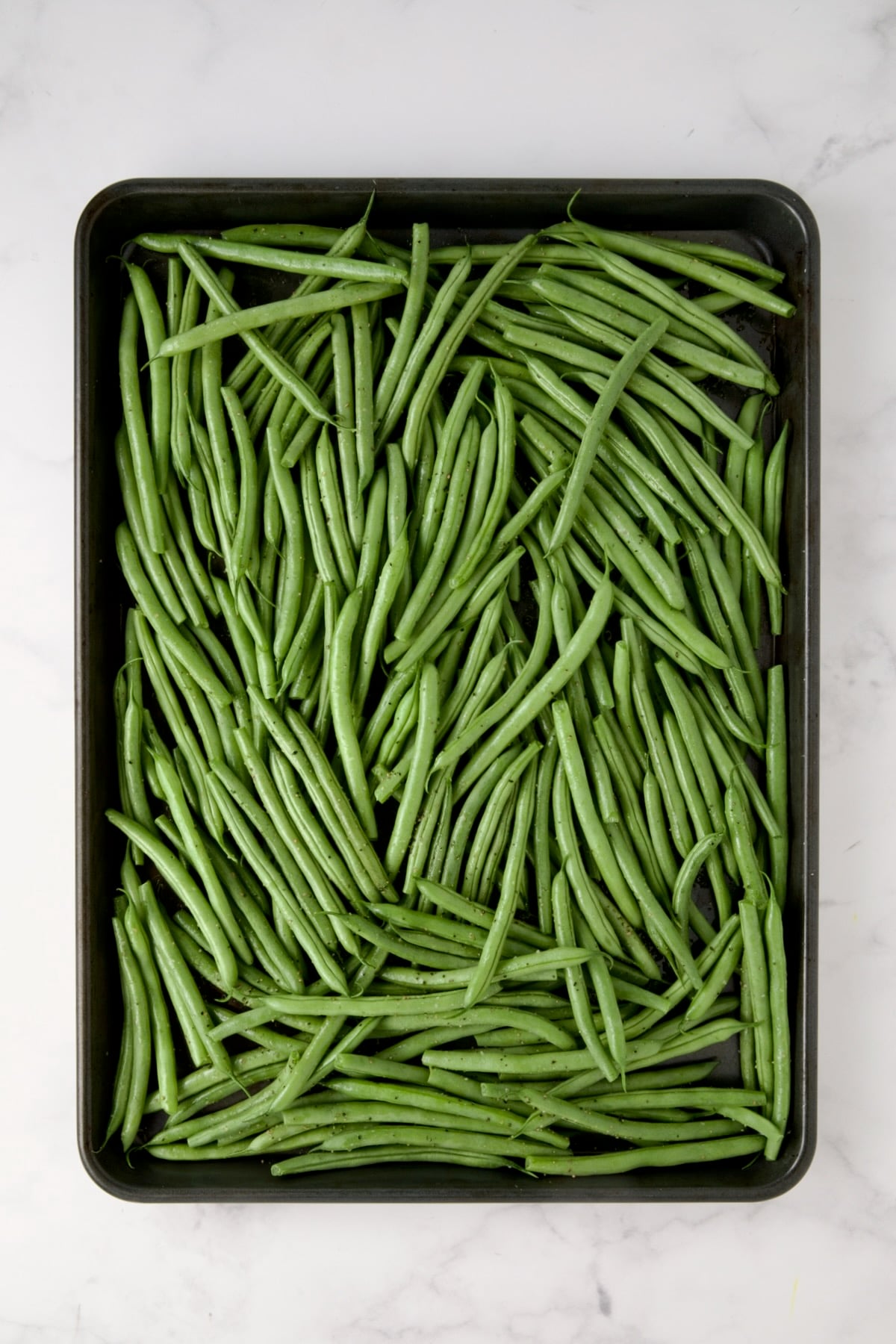 Fresh green beans on rimmed sheet pan before being roasting.