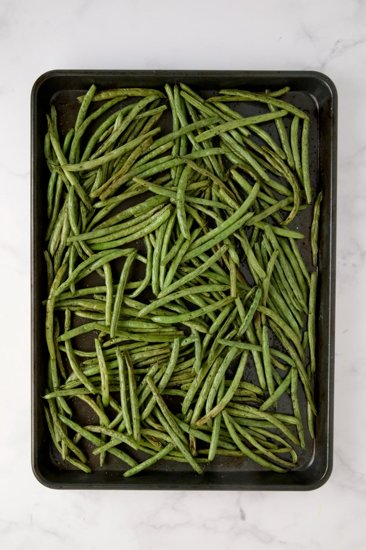 Roasted green beans on rimmed sheet pan.
