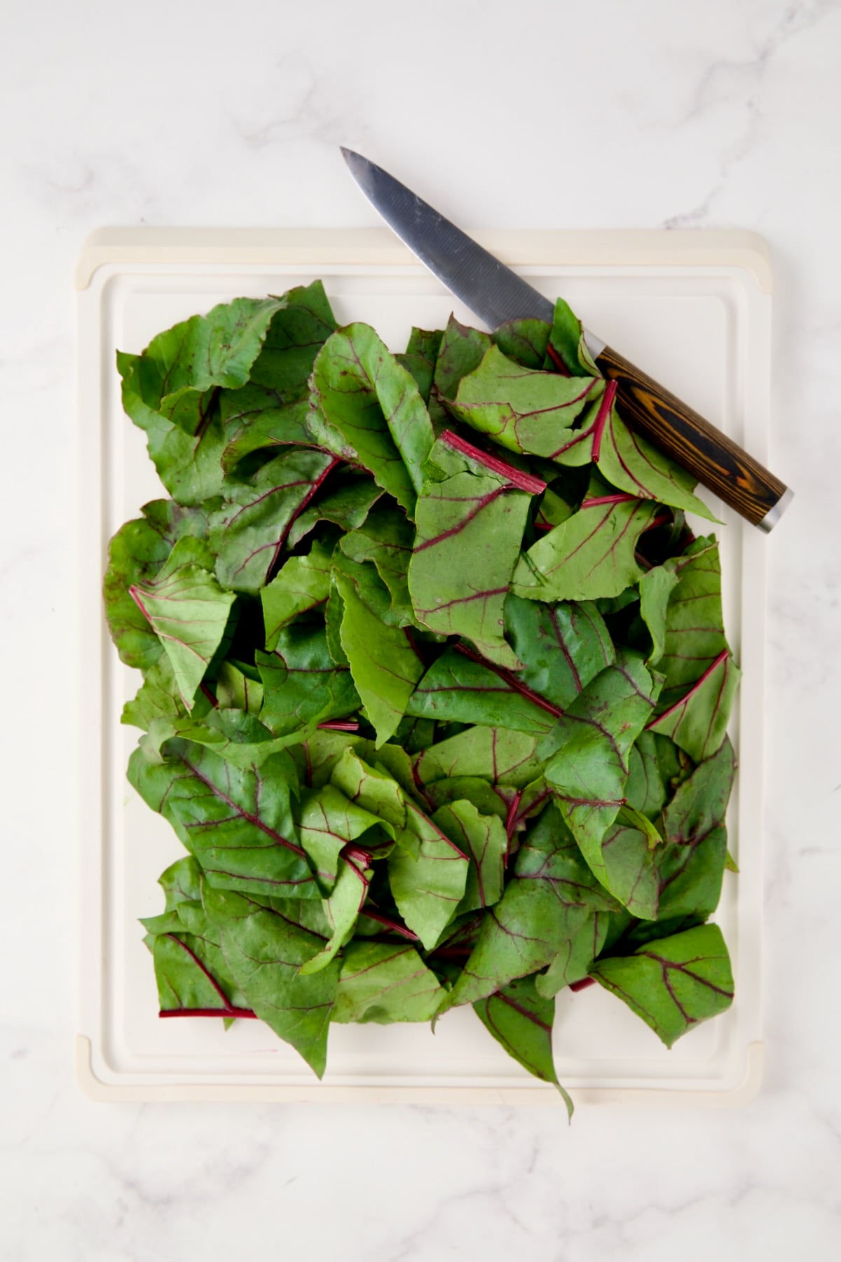 Coarsely chopped beet greens on white cutting board.