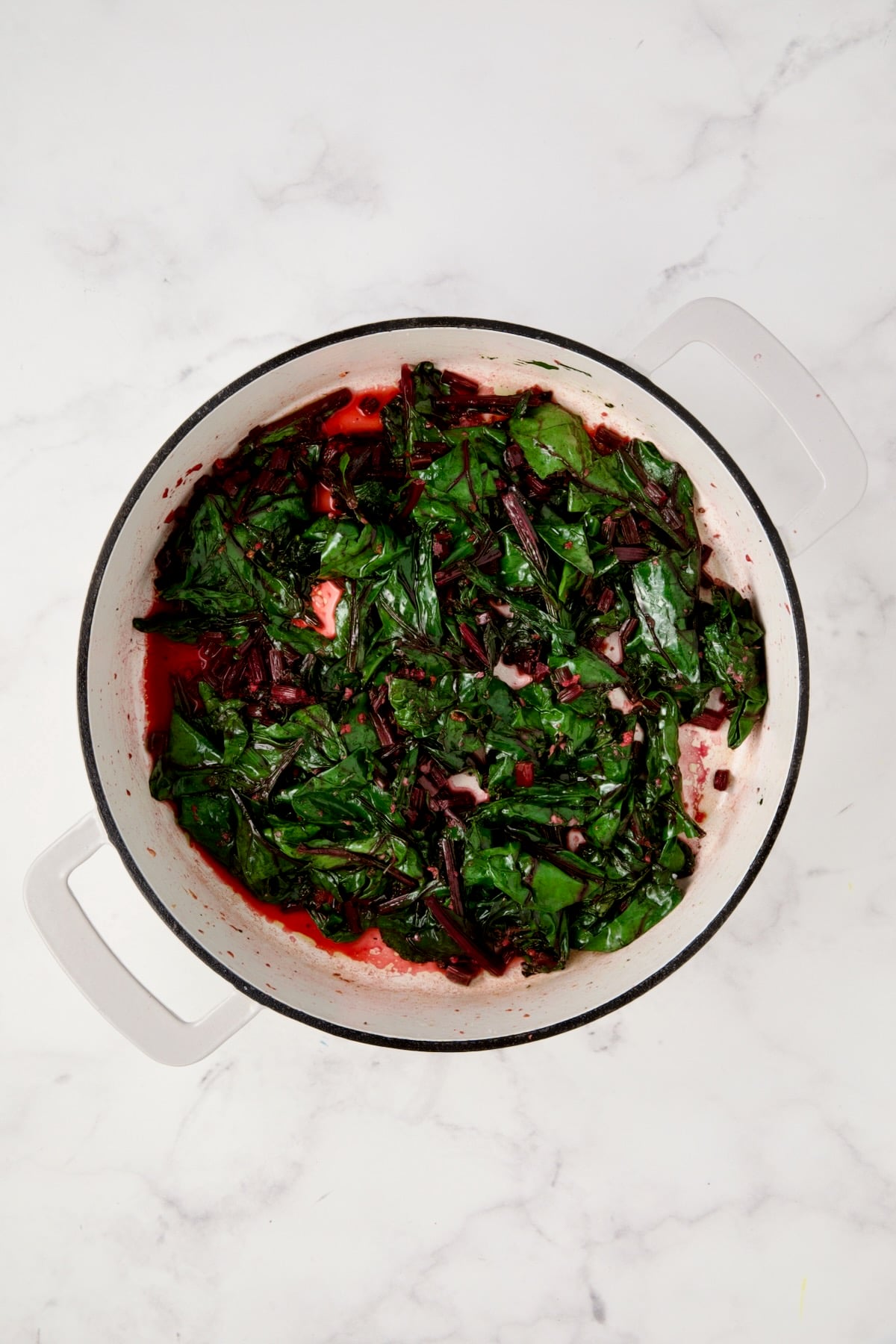 Cooked beet greens in white enamel cast iron skillet.