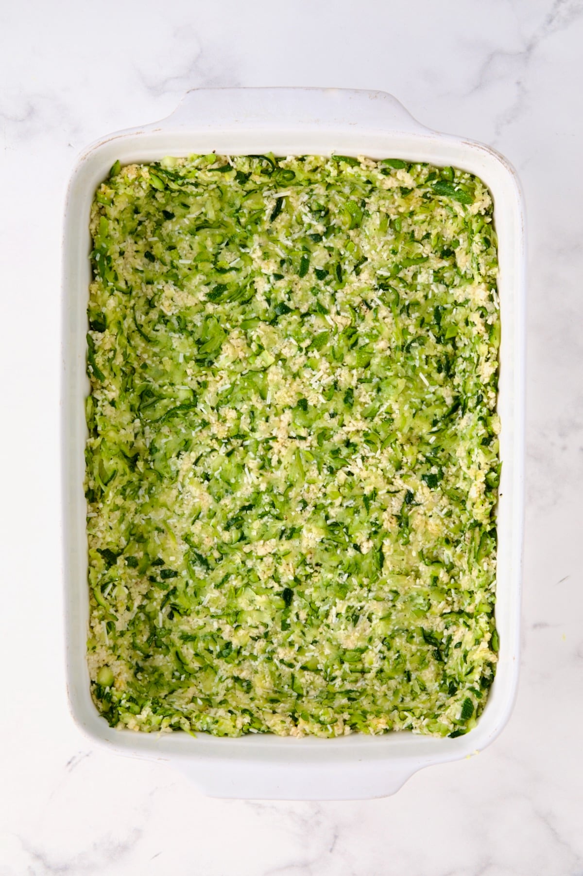 Zucchini crust in white rectangular baking dish before being baked.