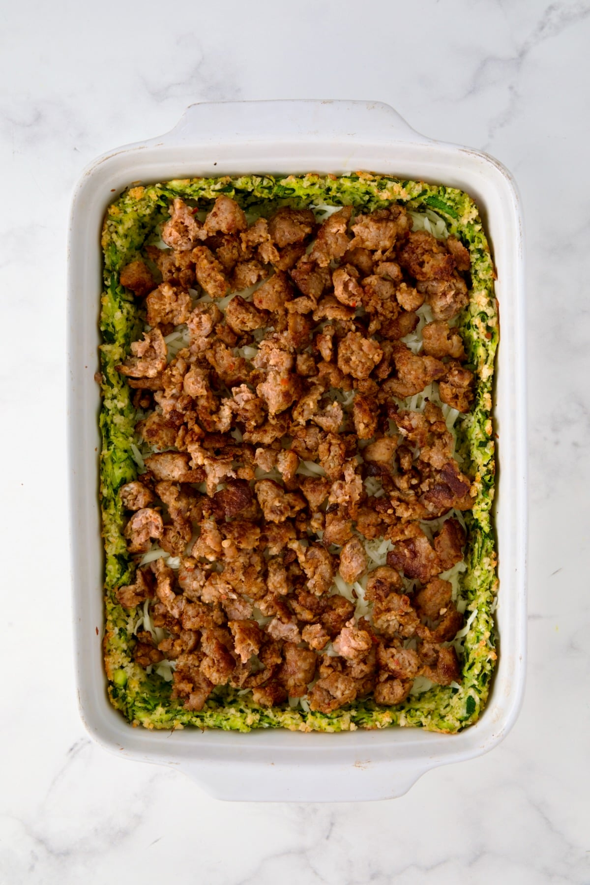 Italian sausage placed over cheese layer in white rectangular baking dish.