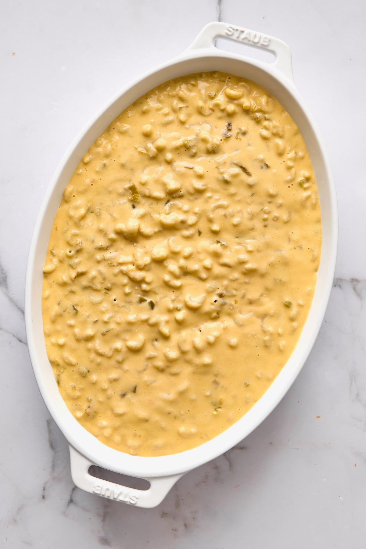 Mac and cheese in white oval baking dish before breadcrumbs are added.