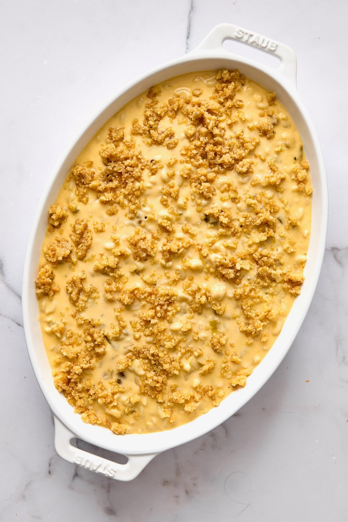 Mac and cheese in white oval baking dish after breadcrumbs are added.