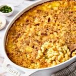 Hatch Green Chili Mac and Cheese in oval baking dish with some being scooped out with wooden spoon.