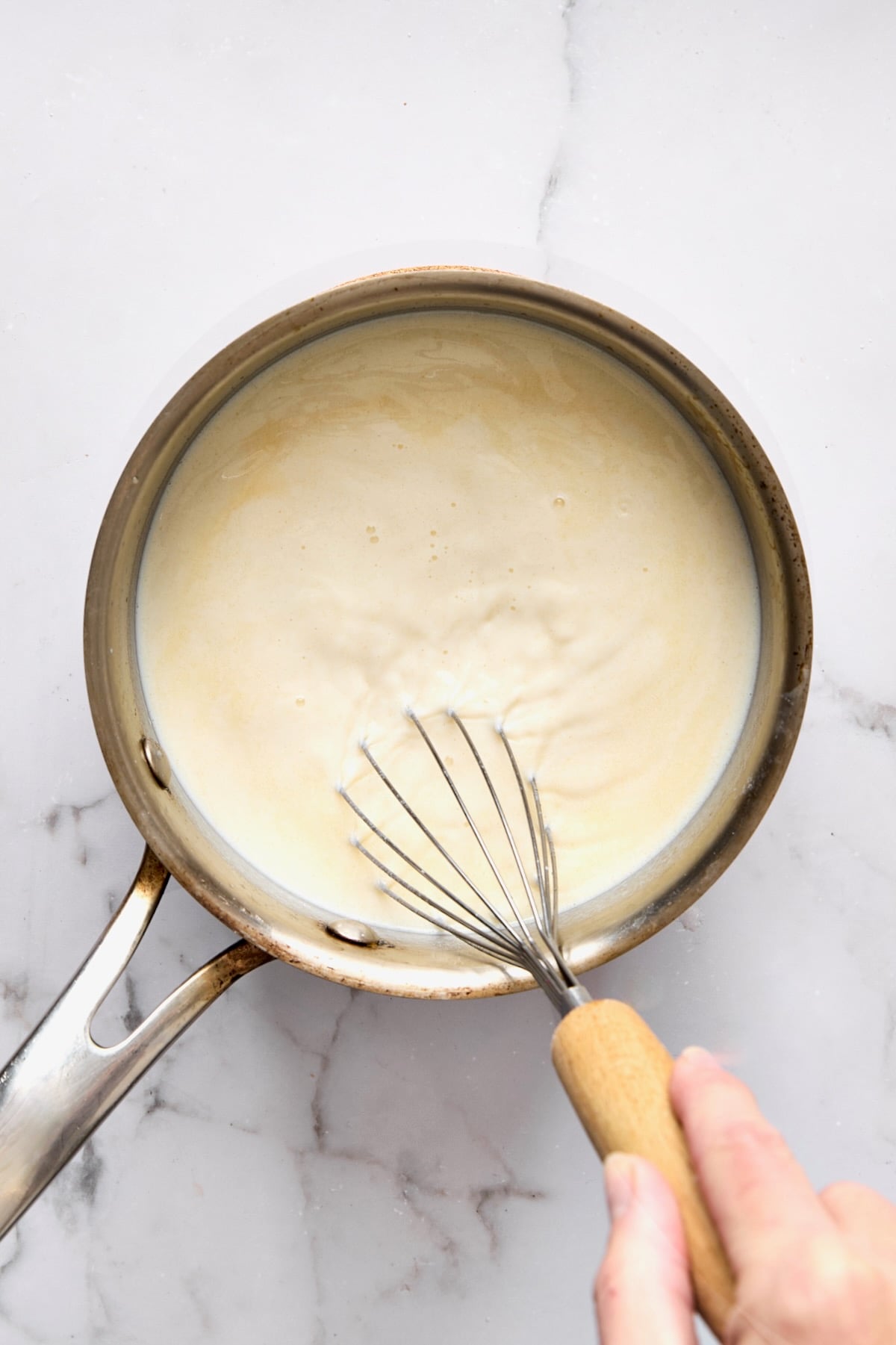 Milk added to butter and flour being whisked in stainless steel saucepan.