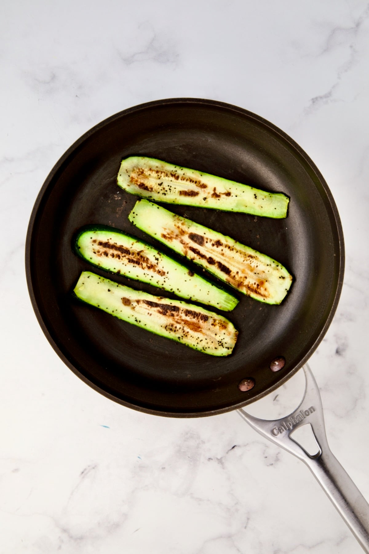 Four charred zucchini slices in nonstick skillet.