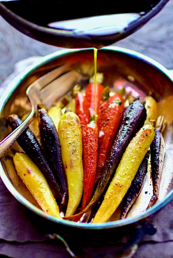 Curry Roasted Carrots in stainless roasting pan with butter being drizzled over.