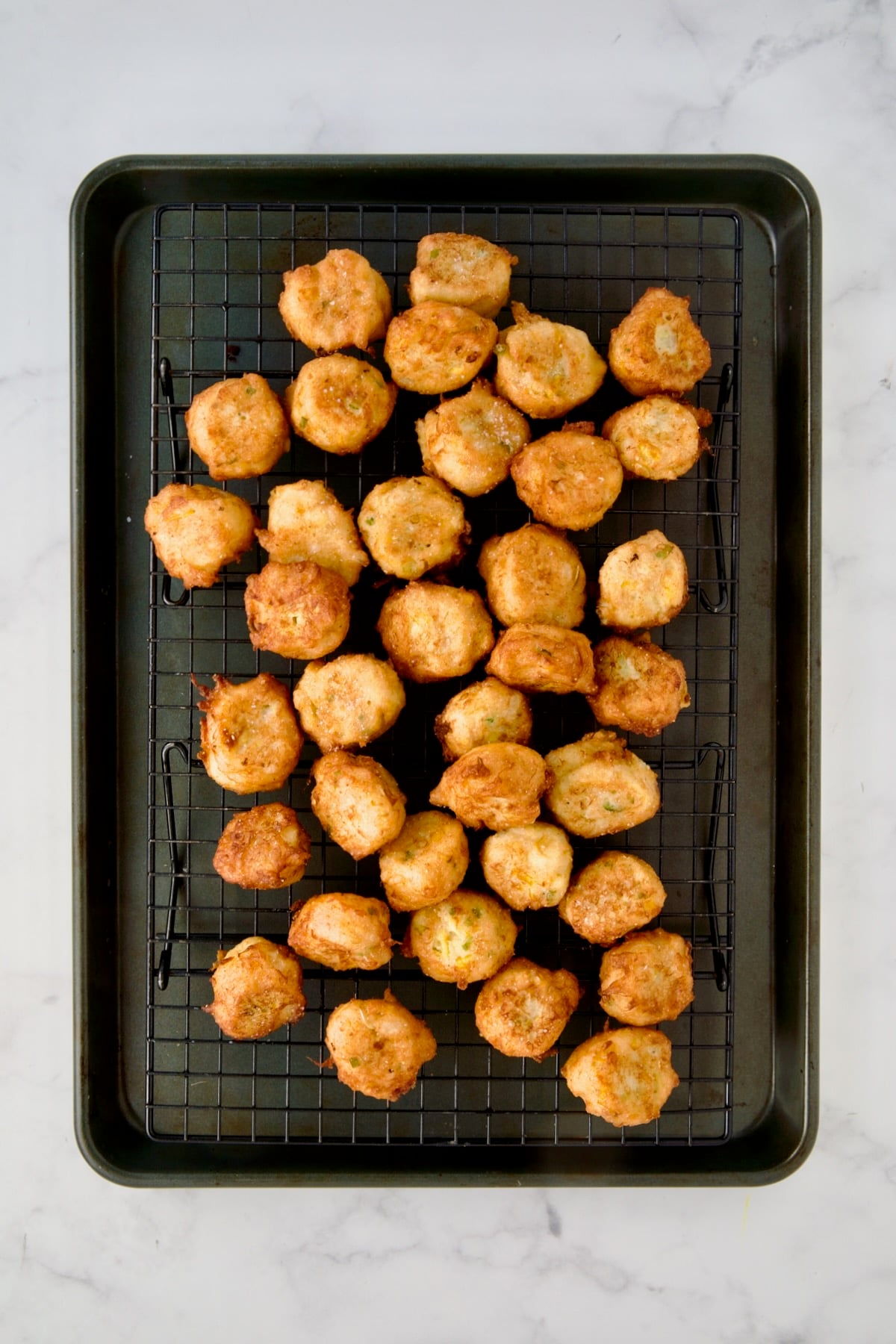 Fried squash puppies on wire rack set over a rimmed sheet pan.