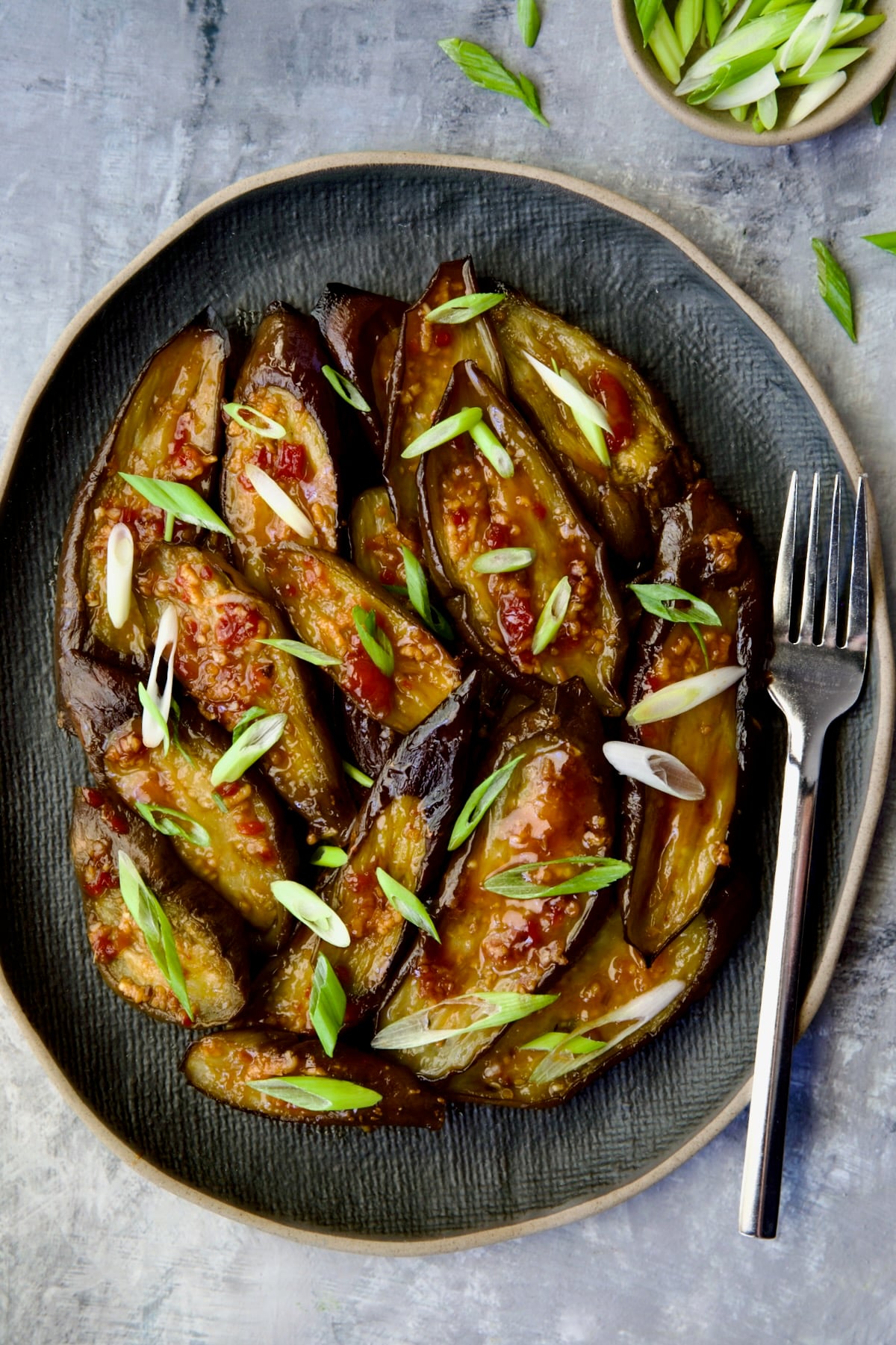 Thai Sweet Chili Eggplant on blue oval plate with fork garnished with scallions.