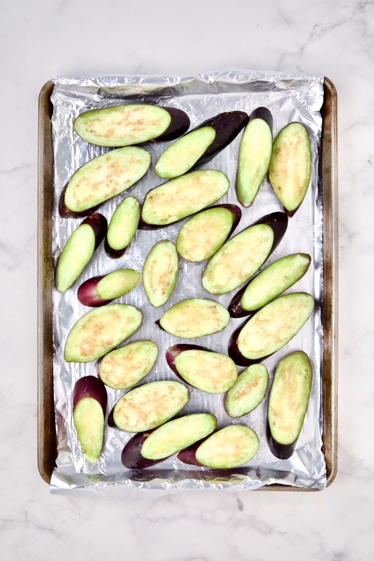 Sliced eggplant on aluminum-foil lined rimmed sheet pan before being baked.