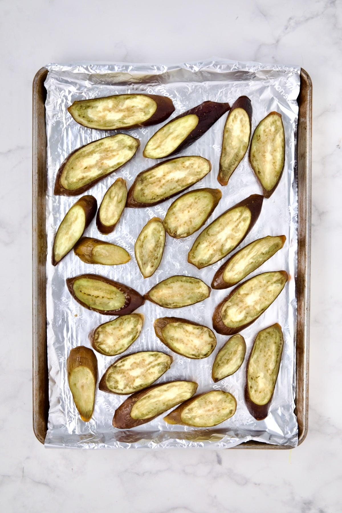 Sliced eggplant on aluminum-foil lined rimmed sheet pan after being baked.