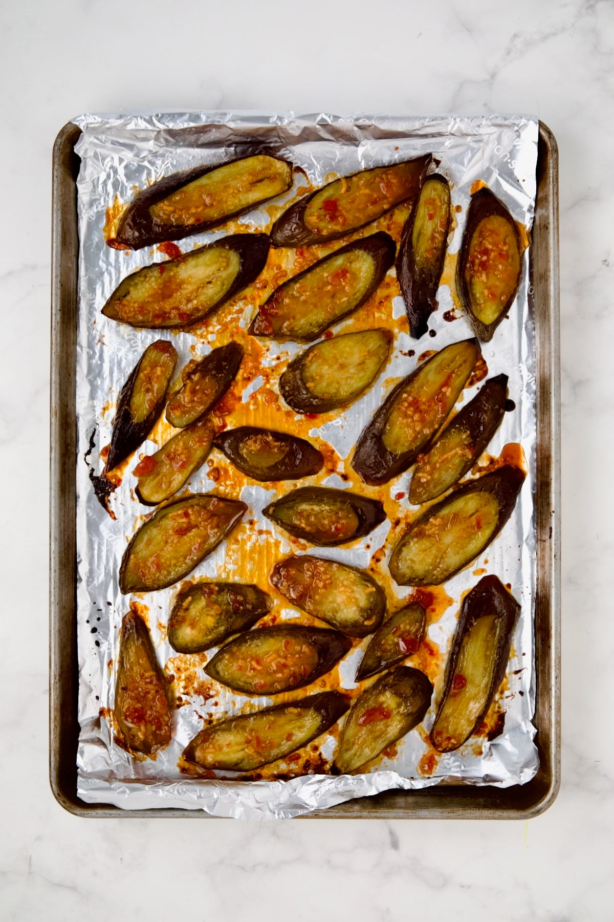 Sliced eggplant on aluminum-foil lined rimmed sheet pan after being broiled.