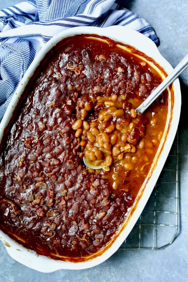 Baked beans in white oval baking dish with serving spoon.