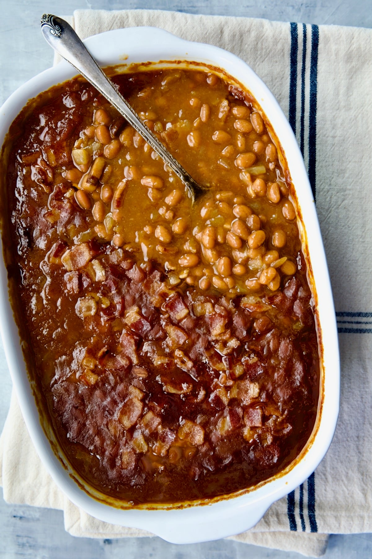 Best Canned Baked Beans Recipe in oval white baking dish with serving spoon.