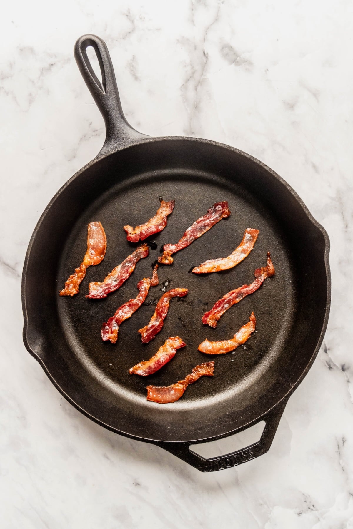 Small cooked strips of bacon in cast iron skillet.