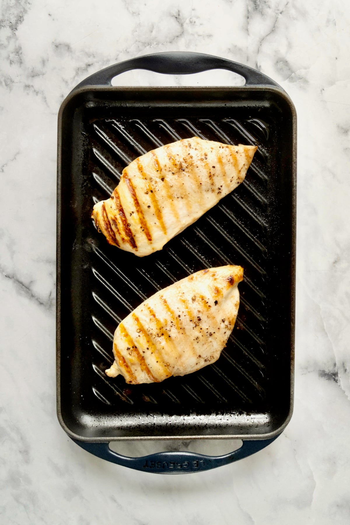 Two grilled boneless skinless chicken breasts on cast iron stovetop grill.