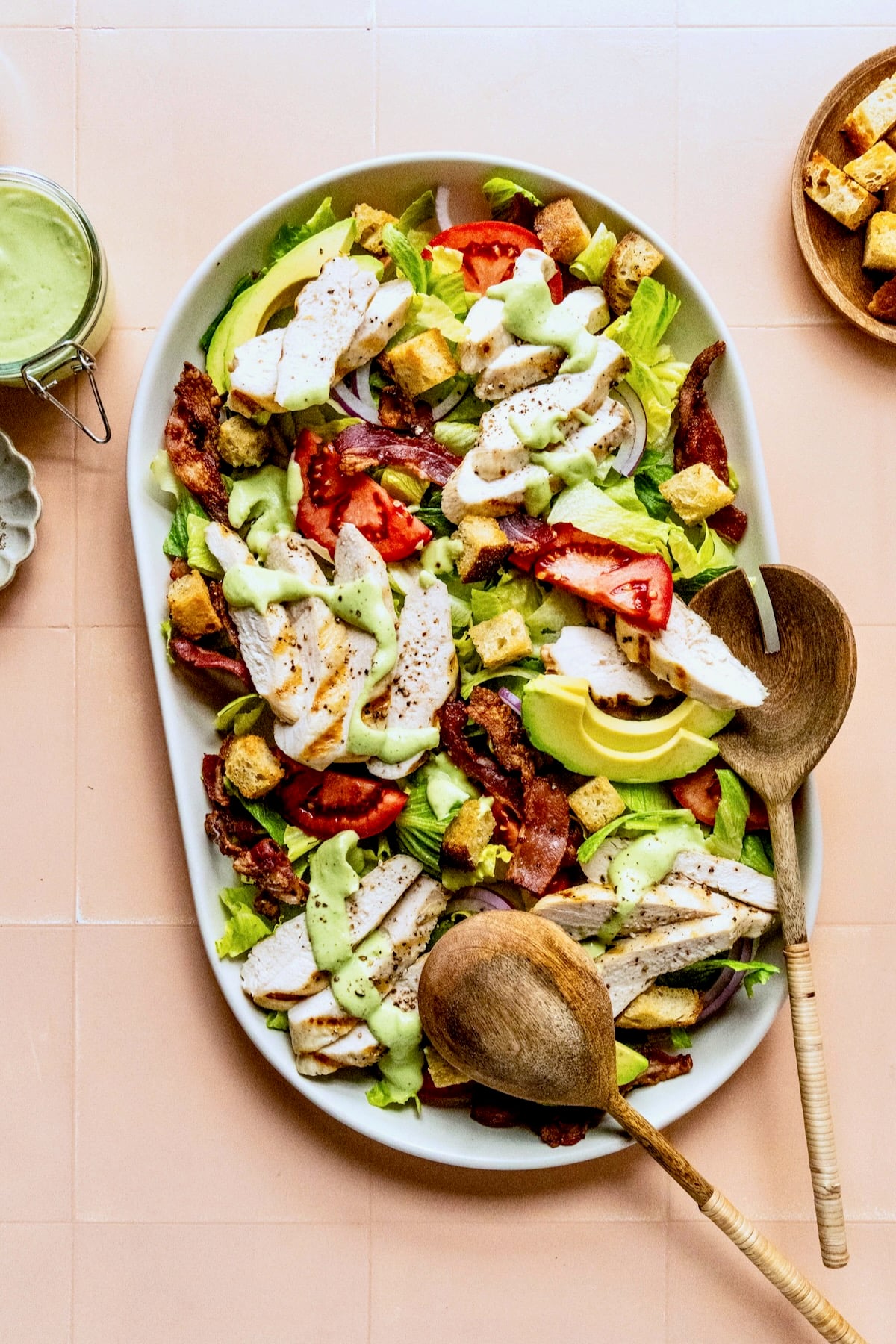 Chicken BLT Salad on white platter with serving utensils.