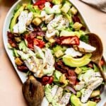 Chicken BLT Salad on oval white platter with wooden serving utensils.