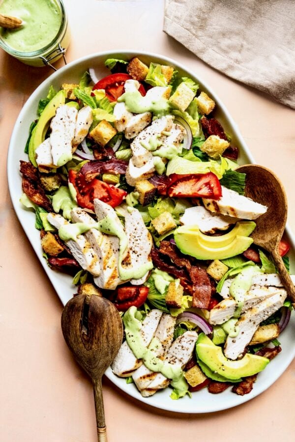 Chicken BLT Salad on oval white platter with wooden serving utensils.