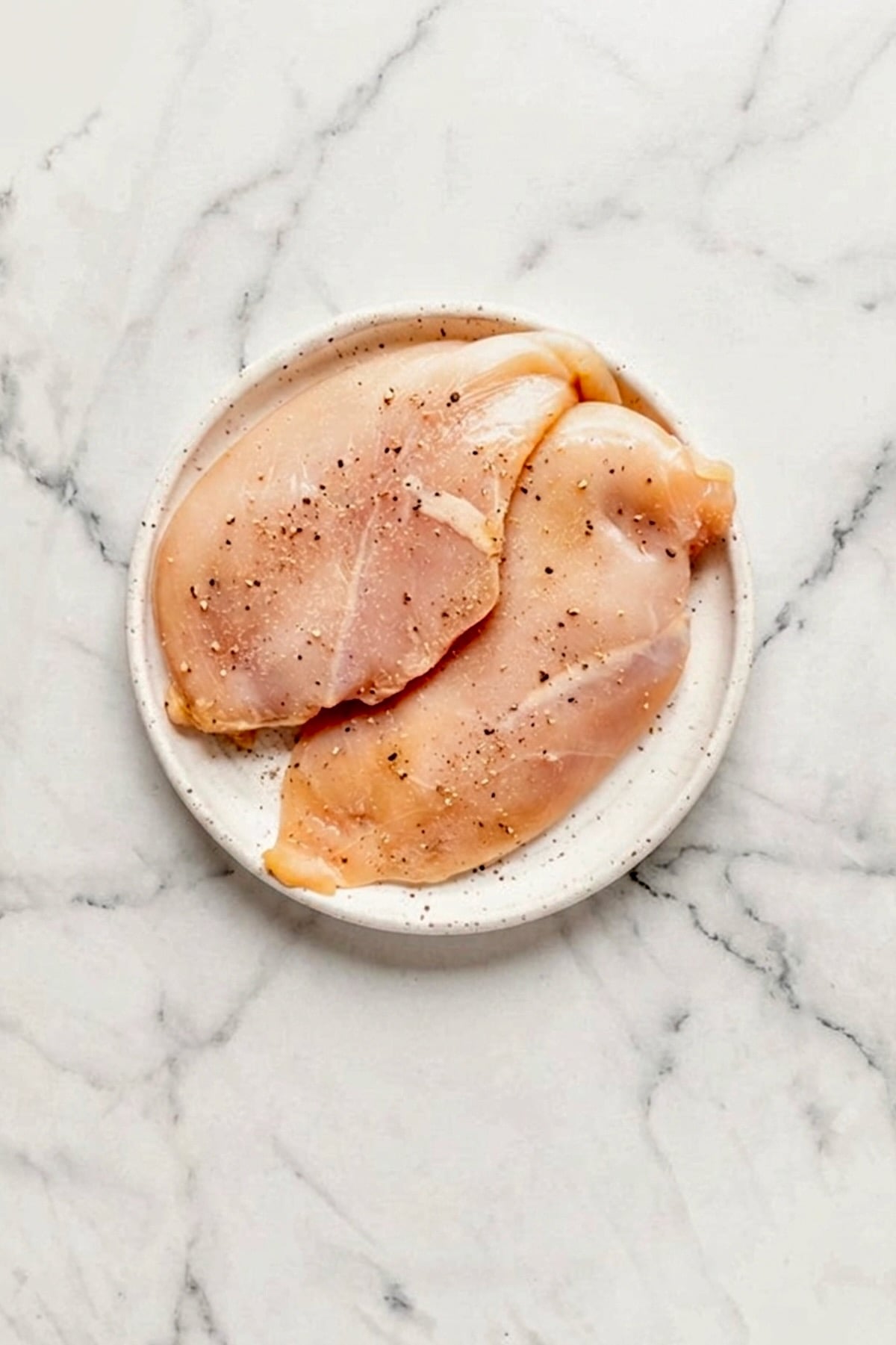 Two boneless skinless chicken breasts on round white plate.