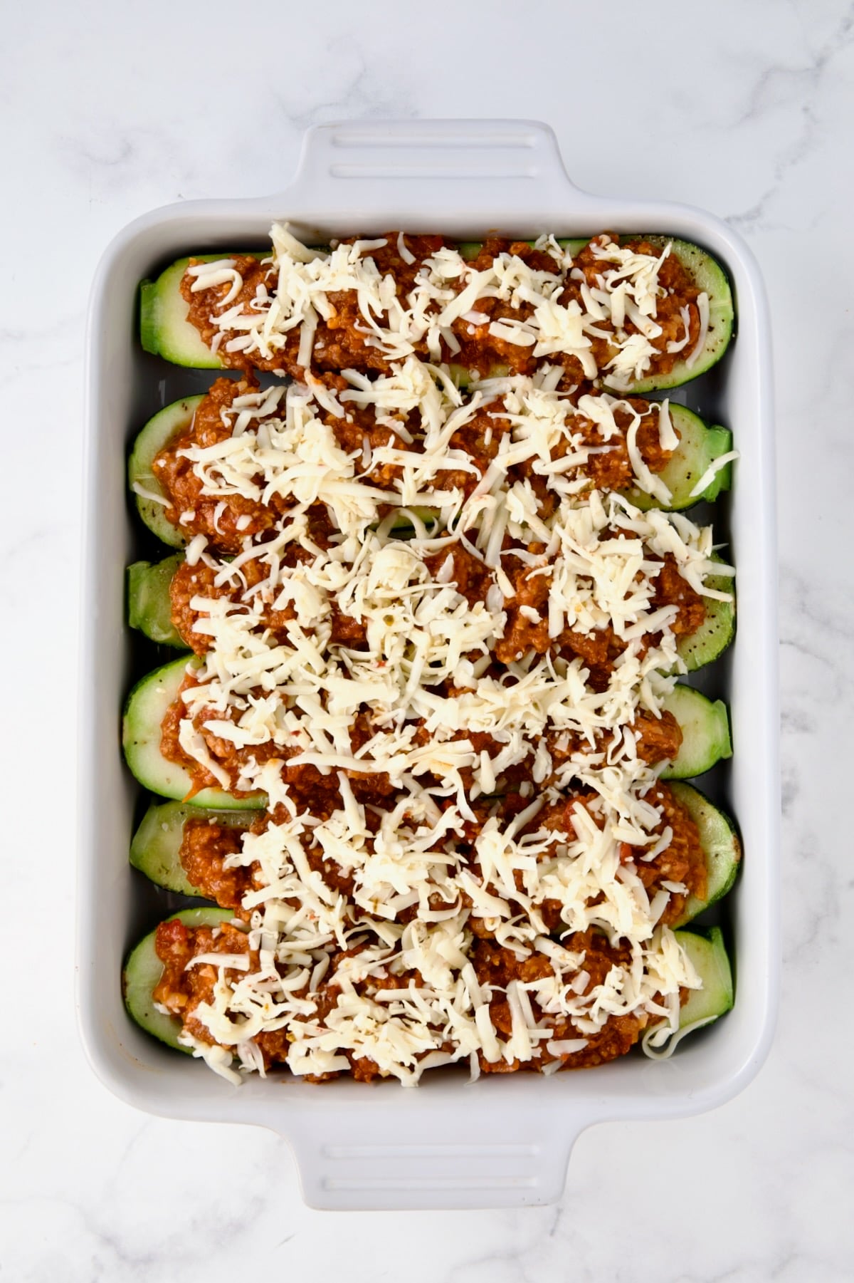 Six Chorizo-Stuffed Zucchini in white rectangular baking dish before being baked with cheese is added.