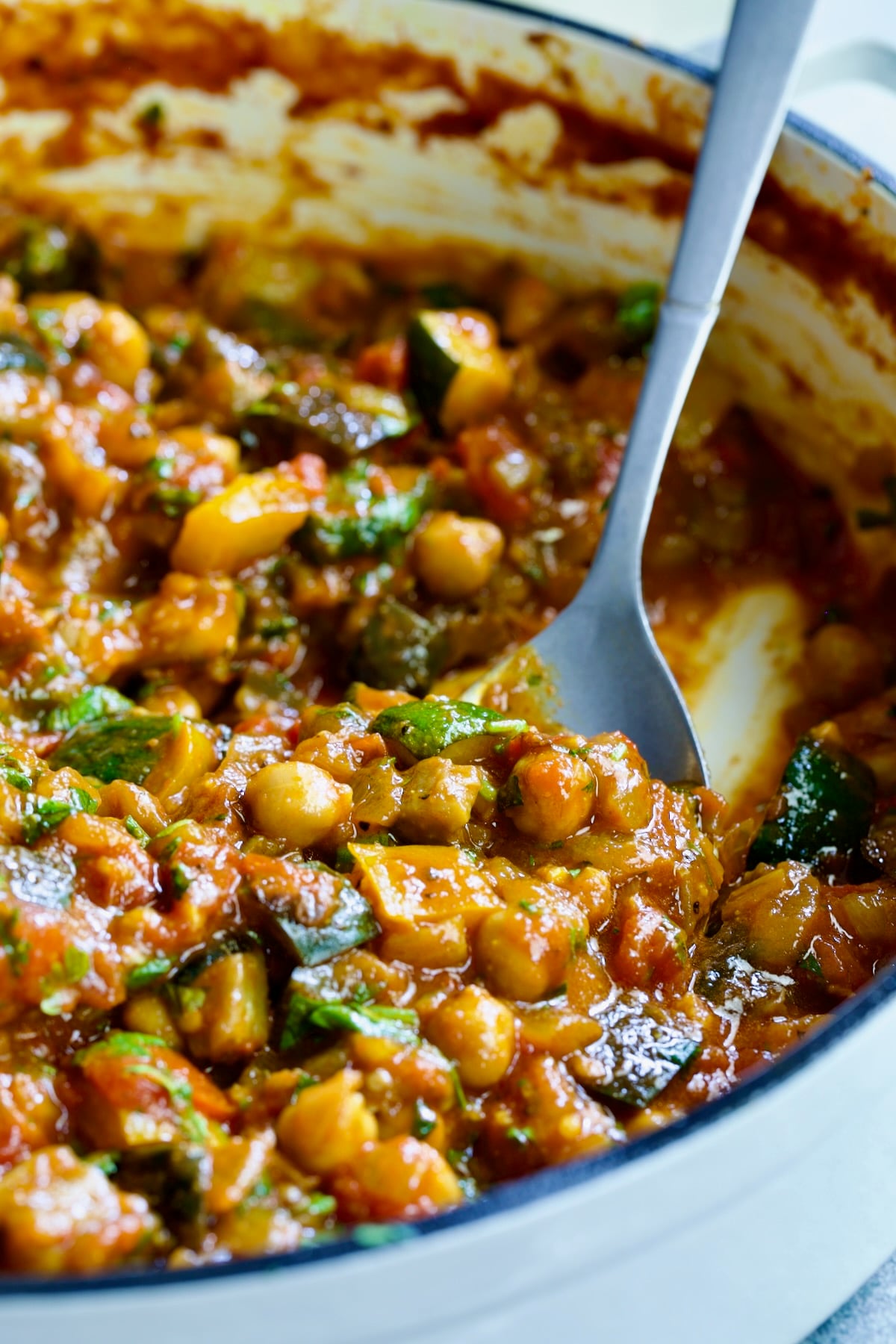 Moroccan Eggplant Stew in white enamel cast iron skillet with spoon scooping some up.