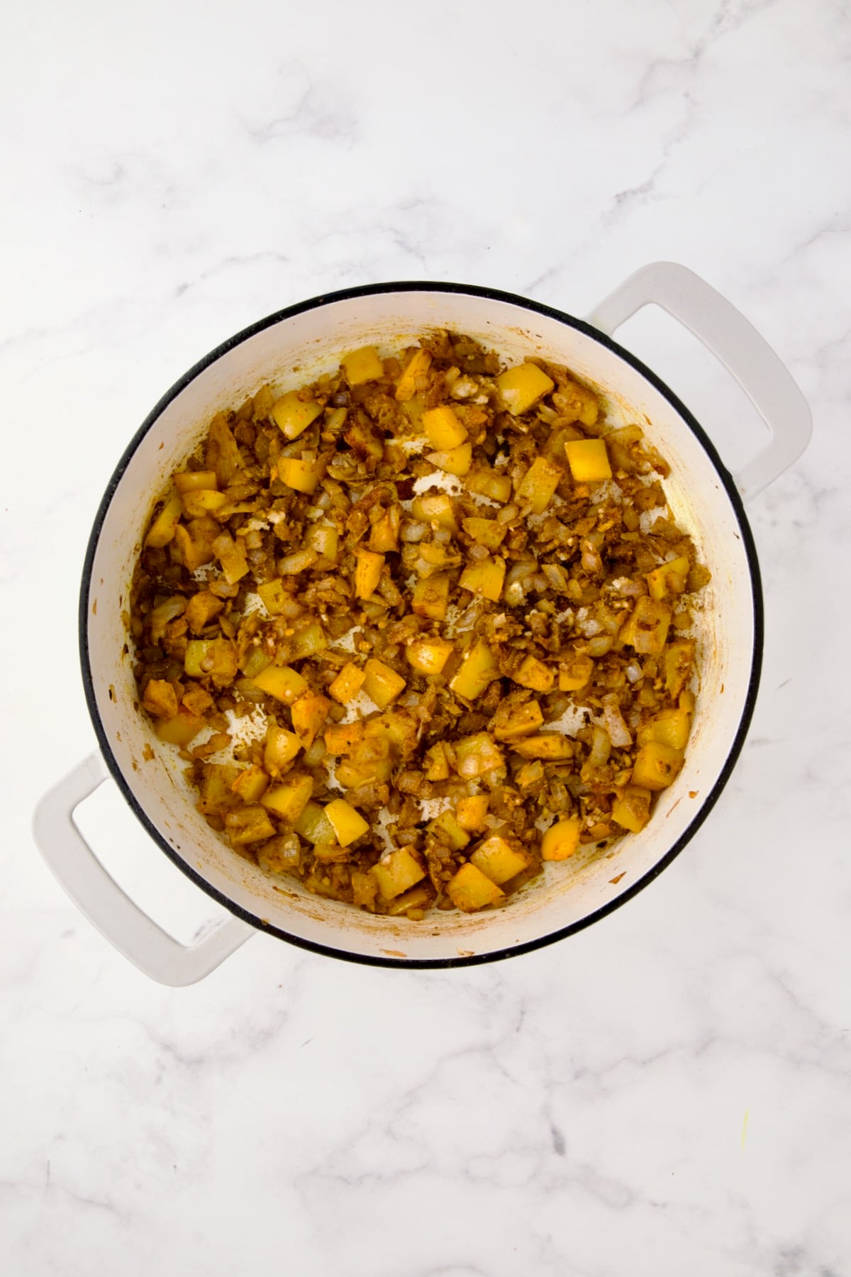 Sauteed spices mixed into onions and yellow bell pepper in white enamel cast iron skillet.